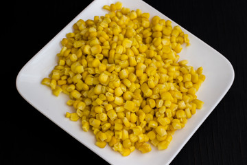 Boiled corn on a white plate. Black background.