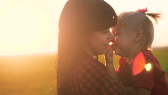 happy family funny a mom holds daughter in her arms slow motion. little lifestyle girl and woman mom kiss hug and play on the field outdoors. teamwork happy family mom takes care of daughter childhood