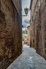 Fototapeta na wymiar Cobbled Alley between Old Buildings In Siena Italy