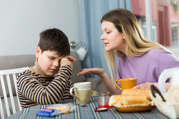 Sad son and unhappy mom having quarrel during breakfast indoors