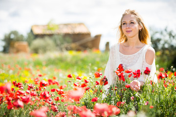Woman wearing  white dress in poppy field and enjoying summer day