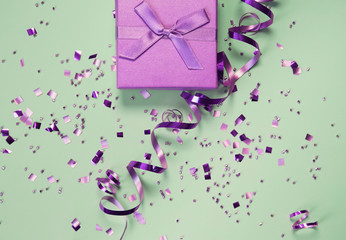 Present box on mint background with shiny confetti. Holiday and festive backdrop. Flat lay style