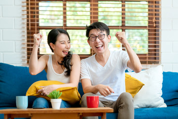 celebrate successful with exited of asian marry couple family hand touch together on sofa watching sport game on tv home interior background