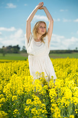 Naklejka na ściany i meble Young woman in yellow oilseed rape field stretch oneself outdoor