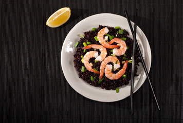 Cooked black rice with shrimps and green onion in a plate on the black background.