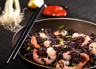 Cooked black rice with shrimps and green onion in a pan on the black background.