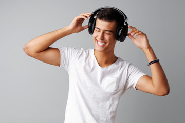 Young man teenager listening to music with his headphones over a grey background