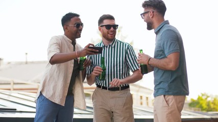 leisure, technology and people concept - happy male friends with smartphone drinking beer and talking at rooftop party in summer