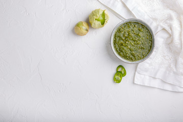 Tomatillo salsa verde. Bowl of spicy green sauce on white table, mexican cuisine. Top view. Copy space. - obrazy, fototapety, plakaty