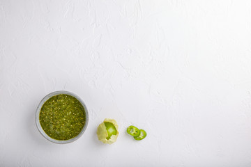 Tomatillo salsa verde. Bowl of spicy green sauce on white table, mexican cuisine. Top view. Copy space.