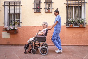 Happy Senior woman with  walking stick in  Wheelchair.with her caregiver at home . They are talking and laughing together.