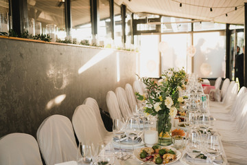 Coziness and style. Modern event design. Table setting at wedding reception. Floral compositions with beautiful flowers and greenery, candles, laying and plates on decorated table.