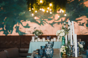 Coziness and style. Modern event design. Table setting at wedding reception. Floral compositions with beautiful flowers and greenery, candles, laying and plates on decorated table.
