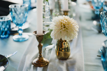 Coziness and style. Modern event design. Table setting at wedding reception. Floral compositions with beautiful flowers and greenery, candles, laying and plates on decorated table.