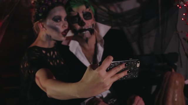 man and woman with Halloween makeup take selfie making frightening faces before celebration party closeup