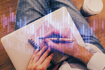 Double exposure of hands writing in notepad with stock market chart.