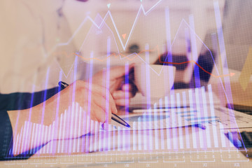 Double exposure of man's hands writing notes of stock market with forex graph.