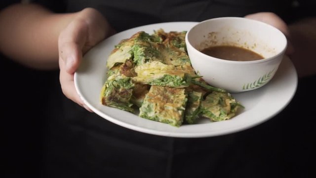 Lady showing Fried egg with Cha-Om on a dish. made from climbing wattle. Thai dish. slow motion.
