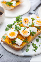 Bruschetta with pumpkin puree, boiled eggs, fresh basil and cream cheese on grey linen textile. Cup of coffee on the background. 