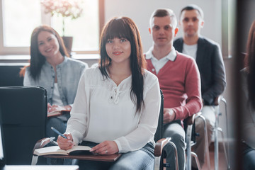 Happy brunette looks at camera. Group of people at business conference in modern classroom at...