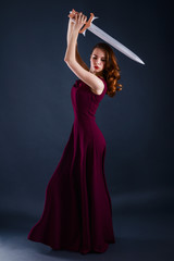 Beautiful young princess in a long dress defending herself with a sword
