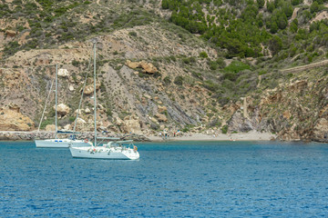 Fototapeta na wymiar Two white yachts on the water near a mountainous shore in a bay near the city of Cartagena in Spain
