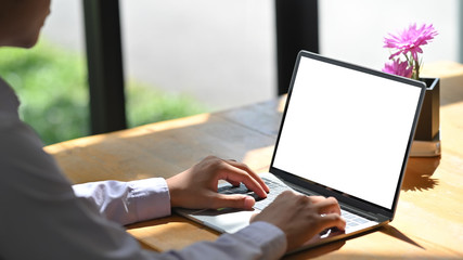 Closeup man typing mockup laptop computer on wood table.