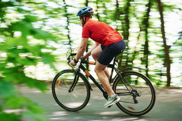 Fototapeta premium Rural scene. Cyclist on a bike is on the asphalt road in the forest at sunny day