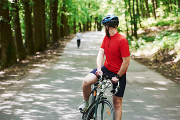 Fototapeta premium Runner behind. Cyclist on a bike is on the asphalt road in the forest at sunny day