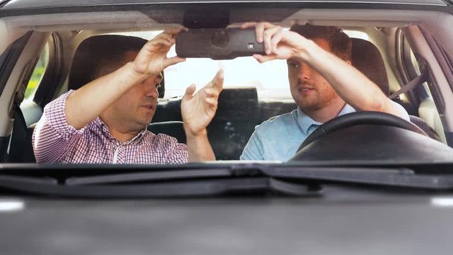driver courses and people concept - man and driving school instructor adjusting mirror and fastening safety seatbelts in car