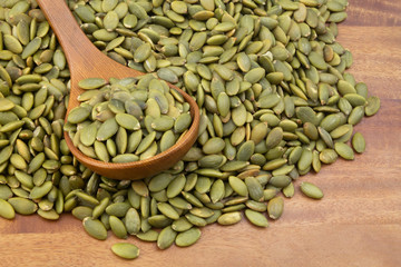Pumpkin seeds and wooden spoon on wooden table