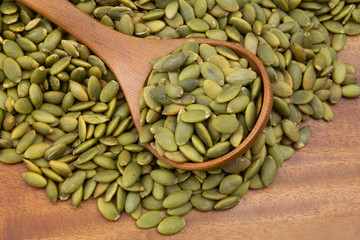 Green pumpkin seeds with wooden spoon on wooden table