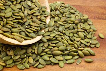 Green pumpkin seeds in wooden bowl and on wooden table