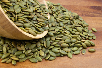 Green pumpkin seeds in wooden bowl and on wooden table