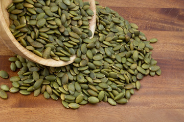 Green pumpkin seeds in wooden bowl and on wooden table