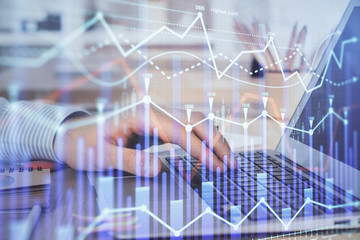 Double exposure of man's hands writing notes with laptop of stock market with forex graph...