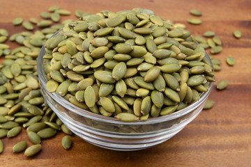 Green pumpkin seeds in glass bowl on wooden table