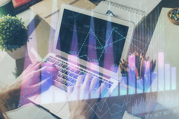Double exposure of man's hands writing notes with laptop of stock market with forex graph background. Top View. Concept of research and trading.
