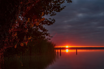 Sunrise - Sunset over a lake with a blurred background and green leaves - 296348883