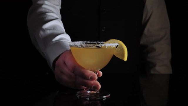 Bartender serves a mixed fresh yellow lemon cocktail margarita drink isolated against black background