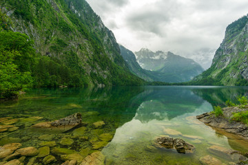 A clear mountain lake with dark clouds and high mountains in the background - 296349612