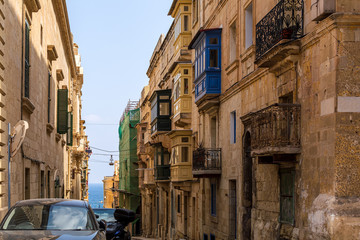 Fototapeta na wymiar Residential house facade with traditional Maltese multicolored enclosed wooden balconies in Valletta, Malta, with sea at background. Authentic Maltese urban scene.