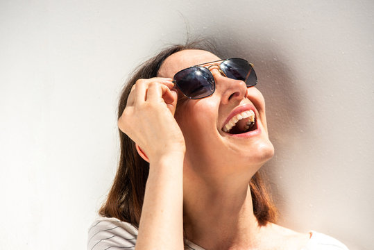 Close up happy older woman laughing with sunglasses by white background