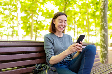 Obraz premium smiling middle aged woman sitting in park with mobile phone