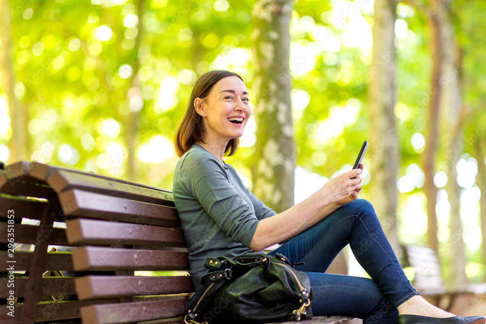 Wall mural  happy older woman sitting in park with mobile phone