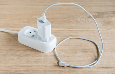 Charger with usb cable for smartphones connected to a power strip. Wood table background.