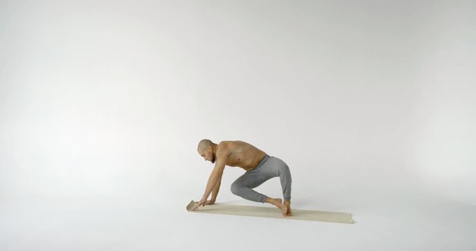 A flexible and plastic male yogi with a beard does yoga on a rug in a white Studio. He does does the plank, the dog-muzzle-up pose and the dog-muzzle-down pose.