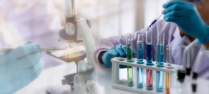Laboratory concept; Scientist use dropper to transfer chemical reagent to test tube. He observe the chemical reaction in laboratory with blurred background of microscope testing