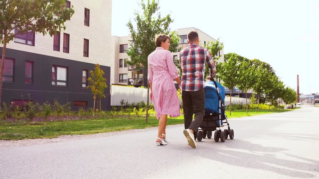 family, leisure and people concept - happy mother and father with little son in stroller walking along city street