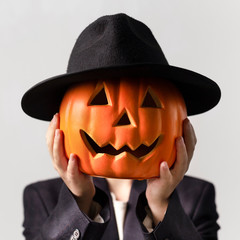 Man holding Jack o Lantern head in black hat over his face